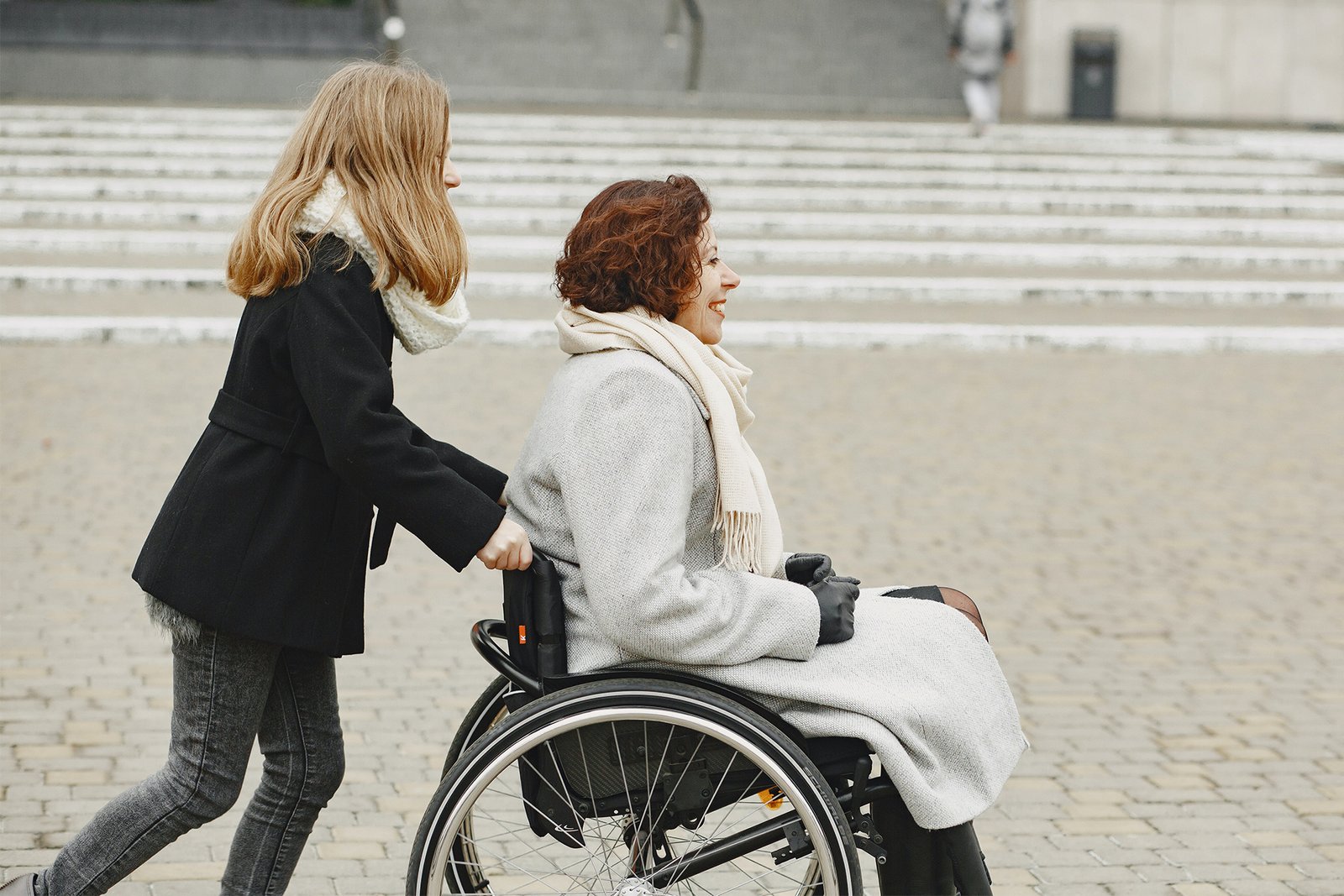 Niña llevando a mujer en silla de ruedas